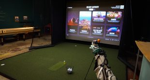 Golfer practicing in an indoor golf simulator with exposed brick walls and a projected fairway.
